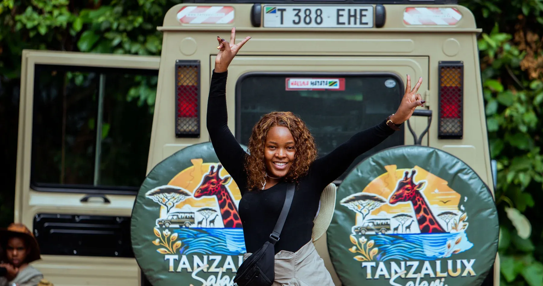A traveller celebrating beside a branded TanzaLux safari vehicle