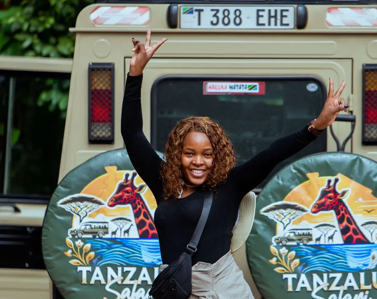 A traveller celebrating beside a branded TanzaLux safari vehicle in Arusha