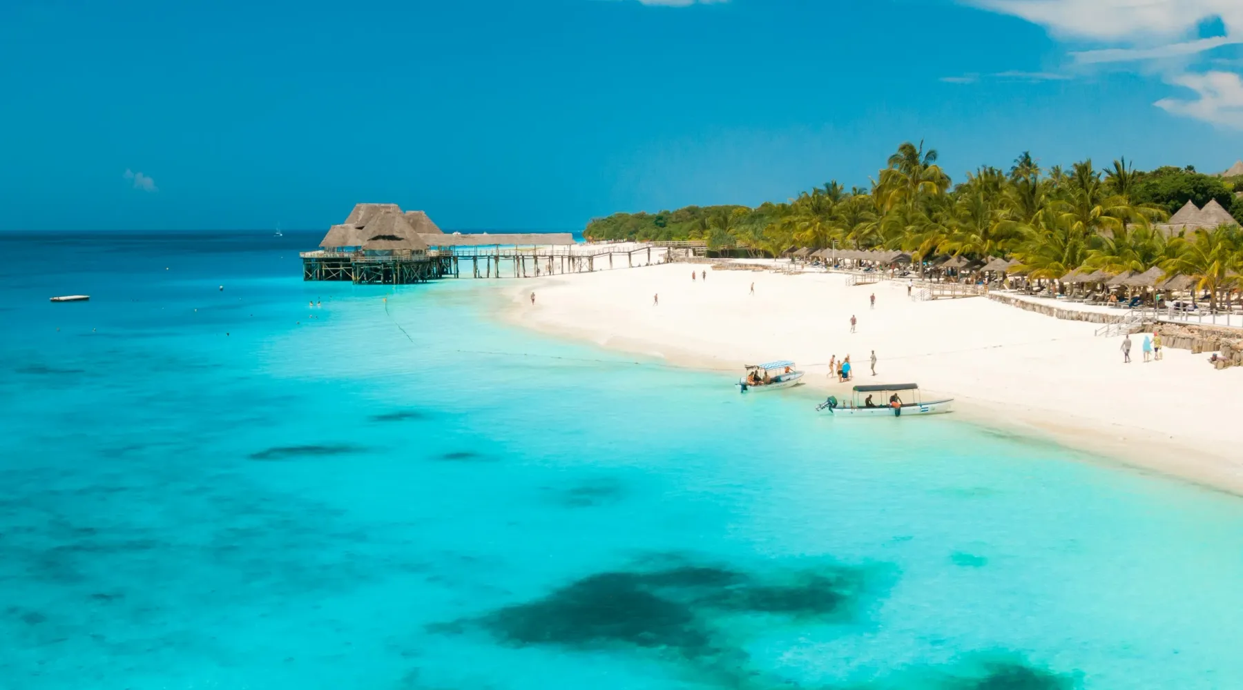 A white-sand Zanzibar beach with a traditional dhow sailboat at sunset
